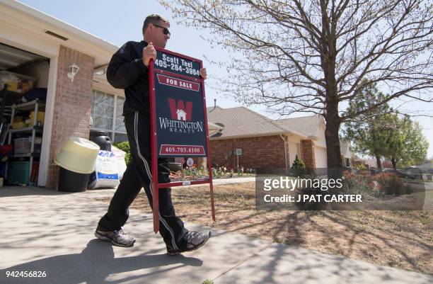 Scott Teel, a high school history teacher, carries a 'for sale' sign, as part of his second job as a real estate agent, in Moore, Oklahoma on April...