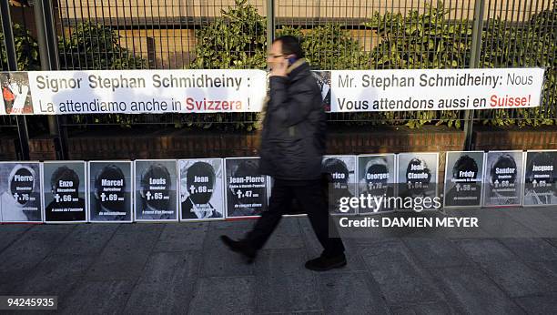 Man walks past banners posted by the Swiss victim association reading 'Mr Stephan Schmidheiny, we are also waiting for you in Switzerland' on Turin's...