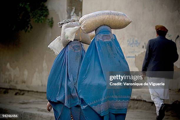 Afghan women have to wear the burqa once they have passed puberty, as pictured here in the streets of Kabul, carrying bags of food on their heads.