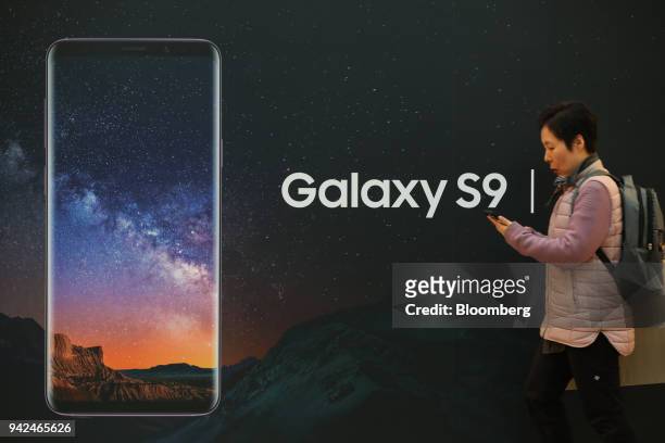 Woman using a mobile phone walks past an advertisement for the Samsung Electronics Co. Galaxy S9 smartphone in Seoul, South Korea, on Thursday, April...