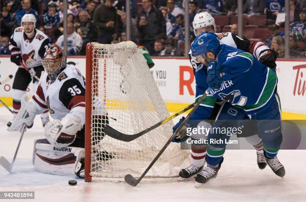 Sam Gagner of the Vancouver Canucks tries a shot on goalie Darcy Kuemper of the Arizona Coyotes while being check by Josh Archibald of the Arizona...