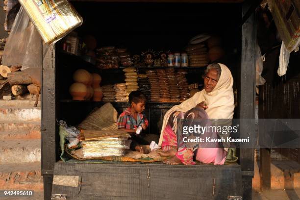 Woman vendor sits in a wooden kiosk with her son in Harish Chandra Ghat on the banks of Ganga River on January 28, 2018 in Varanasi, India. Varanasi...