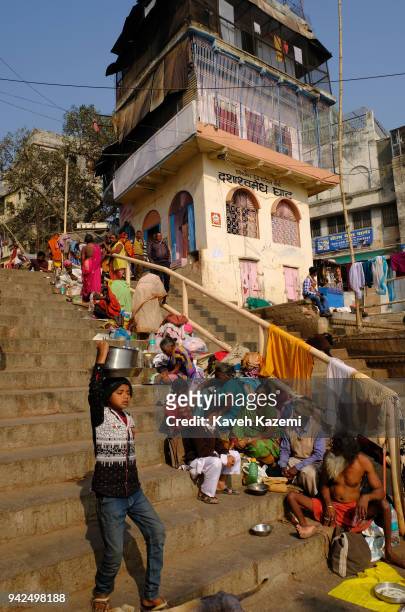Woman beggar sitting on the stairs in a line of people begging talks to her son returning from school on the banks of Ganga River on January 29, 2018...