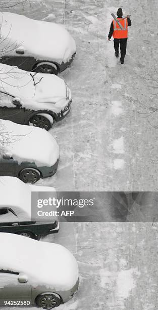 Municpal worker carrying a snow shovel walks past parked cars covered in snow in Moscow on December 8, 2009. Moscow's outspoken mayor blamed...