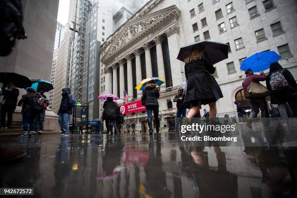 Pedestrians carrying umbrellas walk past the New York Stock Exchange in New York, U.S., on Friday, April 6, 2018. U.S. Stocks fell and Treasuries...