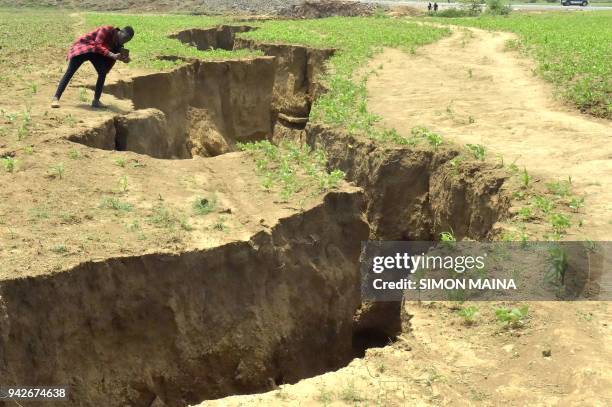 In this photograph taken on April 6 a man takes photograph of a deep chasm in the earth - which has appeared following heavy downpours of rain in...