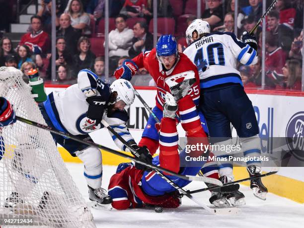 Noah Juulsen of the Montreal Canadiens falls as teammate Jacob de la Rose and Mathieu Perreault of the Winnipeg Jets battle for the puck during the...