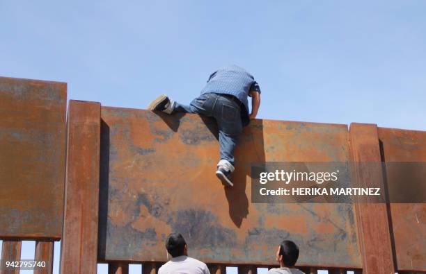 Young Mexicans help a compatriot to climb the metal wall that divides the border between Mexico and the United States to cross illegally to Sunland...