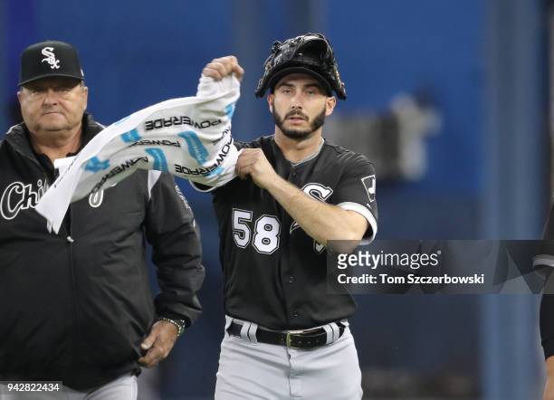 Miguel Gonzalez of the Chicago White Sox wraps a towel around his pitching arm as he makes his way from the bullpen as he walks beside pitching coach...