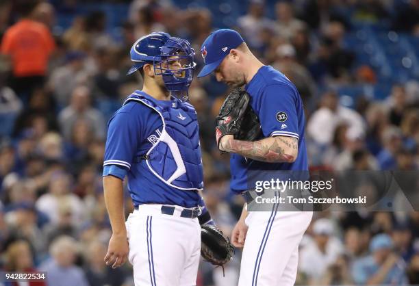 Luke Maile of the Toronto Blue Jays meets on the mound with John Axford in the seventh inning during MLB game action against the Chicago White Sox at...