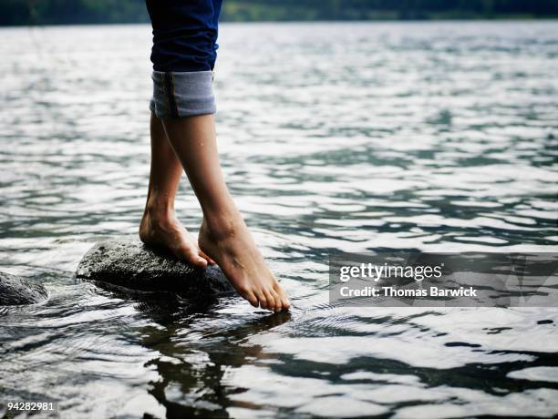 woman standing on rock touching toes to water - testing the water 英語の慣用句 ストックフォトと画像