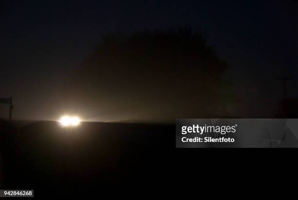 car headlights appear through countryside misty night - silentfoto sheffield stock-fotos und bilder
