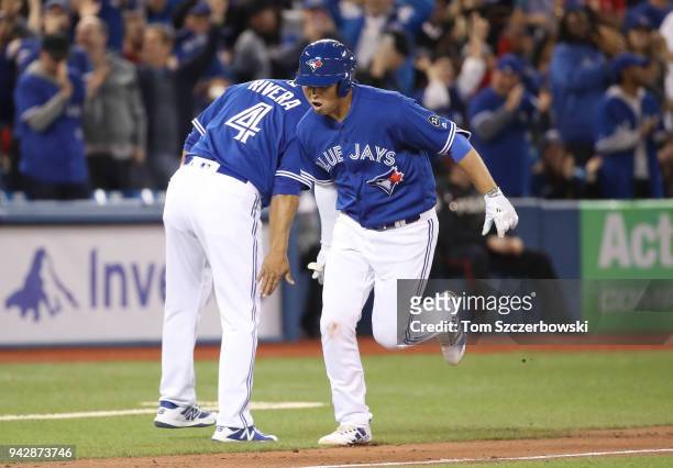 Aledmys Diaz of the Toronto Blue Jays is congratulated by third base coach Luis Rivera as he circles the bases after hitting a solo home run in the...