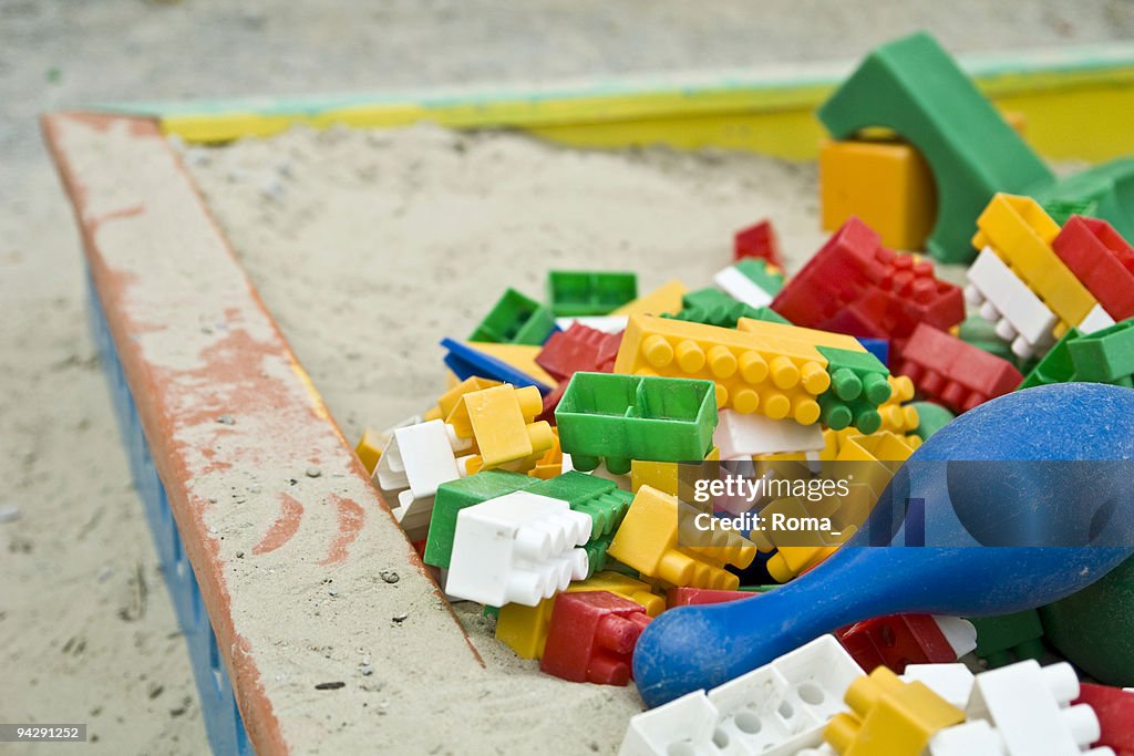 Child's wooden sandbox piled with multicolored plastic block pieces