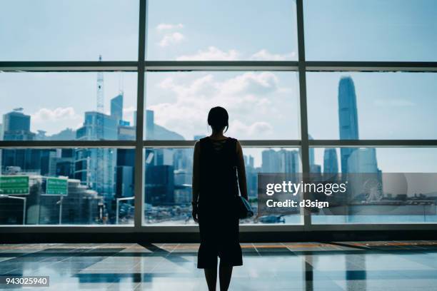 rear view of young executive looking through window to the prosperous city skyline of hong kong - city gegenlicht stock-fotos und bilder