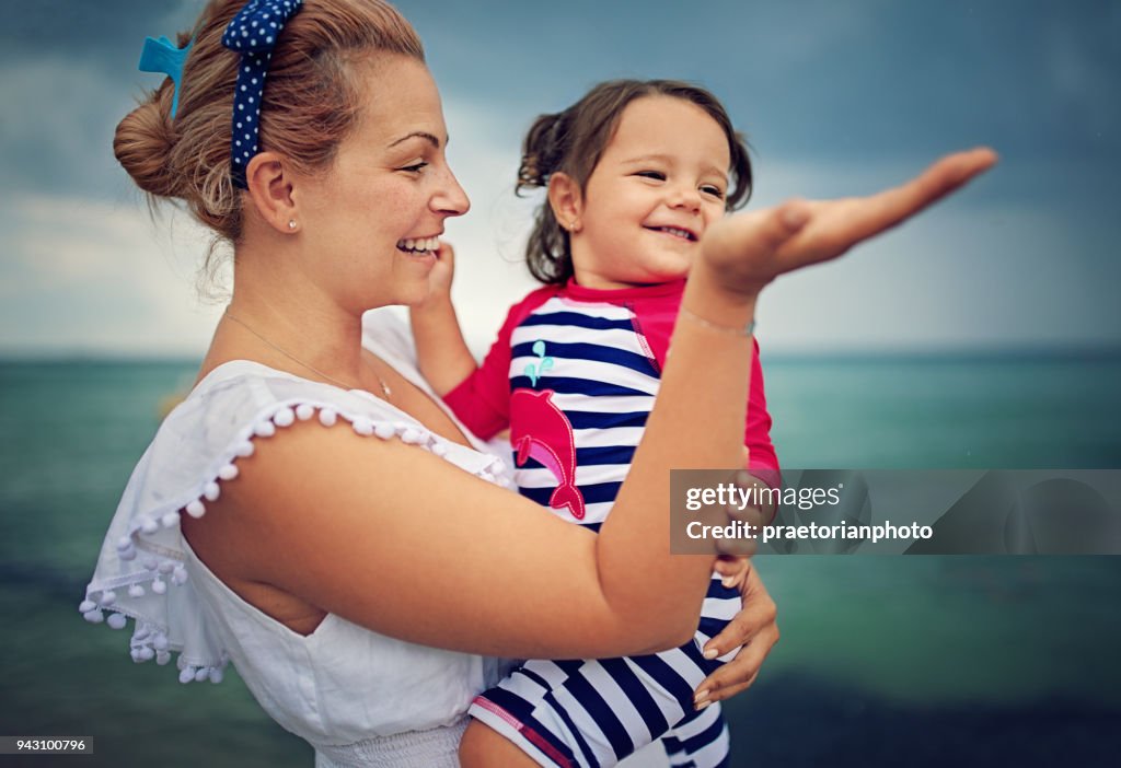 Gelukkig moeder is haar kleine baby knuffelen en genieten van de komende regen over de Oceaan