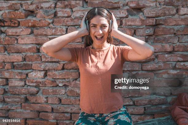 young woman listening to music outdoors on a sunny day - aparelho eletrónico de escuta imagens e fotografias de stock