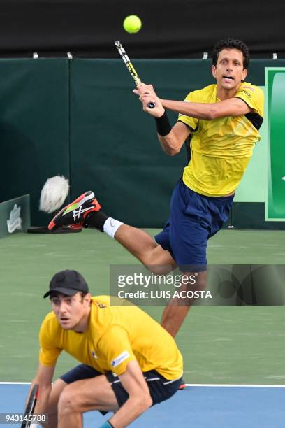 Brazilian tennis players Marcelo Melo returns a ball as teammate Marcelo Demoliner bends against Colombian tennis player Juan Sebastian Cabal and...
