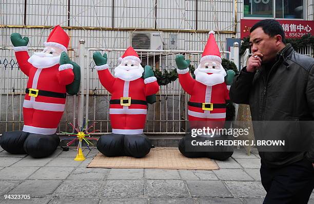 Man walks past a display of inflatable Santa Claus dolls in front of a shop selling Christmas decorations in Beijing on December 12, 2008. China's...