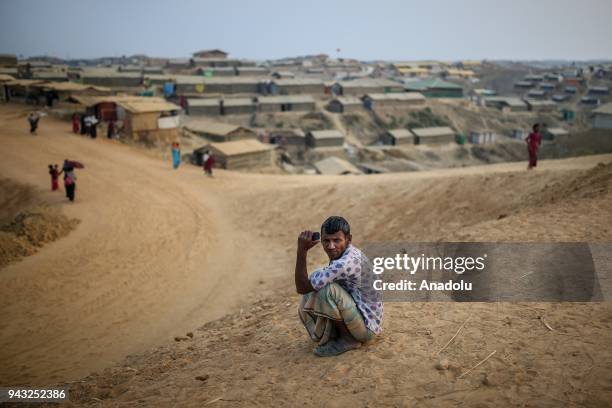 Rohingya man sits on the ground as shelters are seen behind him at Kutupalong refugee camp in Maynar Guna, near Cox's Bazar, Bangladesh on April 07,...