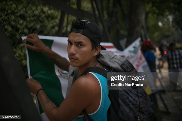 Member of the migrant caravan ties up a Mexican flag over the U-S embassy fence in Mexico City, over Reforma Avenue, on April, 8th 2018.