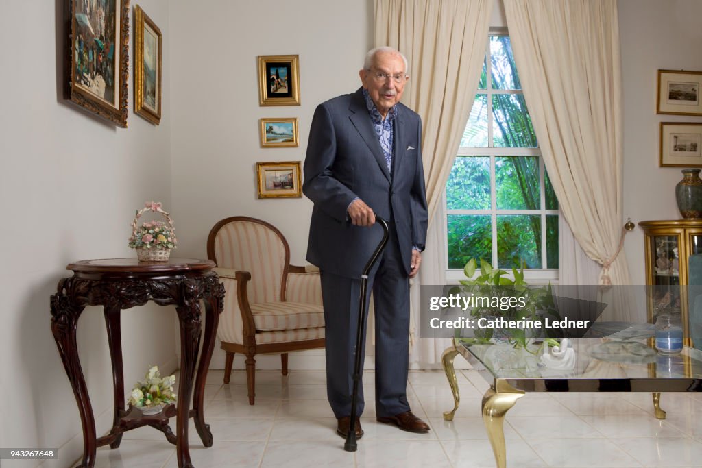 Octogenarian man in suit standing in well appointed living room.