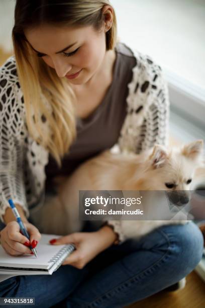young woman with dog sitting on the floor and writting notes - dog pad stock pictures, royalty-free photos & images