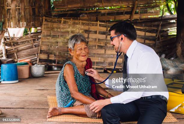 male doctor listening heart beat and breathing of elderly woman - refugee camp stock pictures, royalty-free photos & images