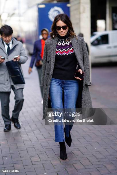 Guest wears sunglasses, a gray coat, a pull over with colored prints patterns, cropped jeans, black shoes, during London Fashion Week February 2018...