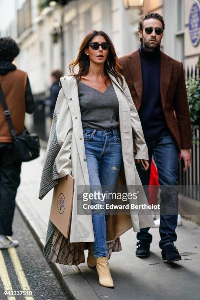 Guest wears sunglasses, a white coat, a gray low neck pull over, blue jeans, beige shoes during London Fashion Week February 2018 on February 16,...