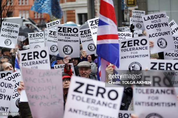 People hold up placards and Union flags as they gather for a demonstration organised by the Campaign Against Anti-Semitism outside the head office of...