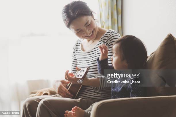 moeder en baby speelt ukulele thuis - teach muziekinstrument stockfoto's en -beelden