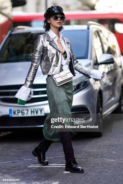 Guest wears a black cap hat, sunglasses, a silver shiny glitter blazer jacket, a green skirt, a white bag, during London Fashion Week February 2018...