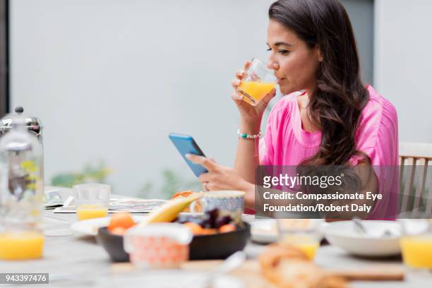 woman using cell phone having breakfast on patio - orangensaft stock-fotos und bilder