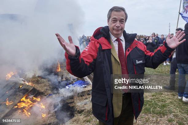 Former UK Indepence Party Leader Nigel Farage stands beside the remains of a small boat on top of a bonfire on the shore during a demonstration in...