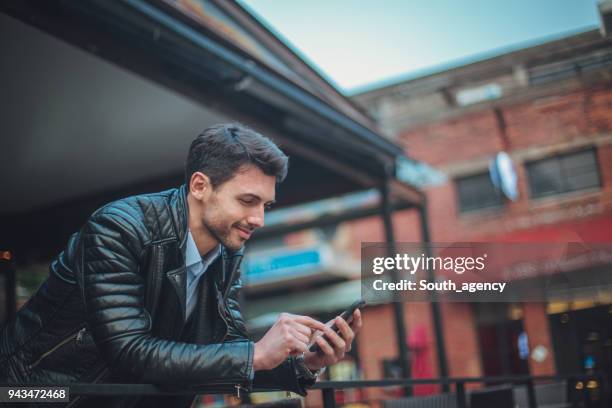 jeune homme à envoyer des sms en plein air - sms'en photos et images de collection