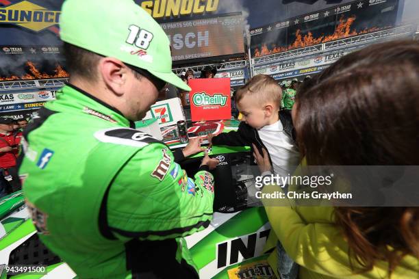 Kyle Busch, driver of the Interstate Batteries Toyota, affixes the winner's decal to his car in Victory Lane with his son Brexton and wife Samantha...