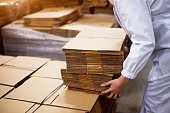 Close up of young female worker picking up stacks of folded cardboard boxes from a bigger stack in factory storage room.