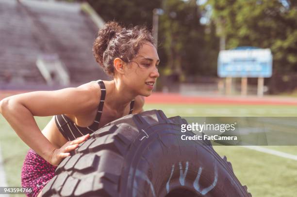 female athlete cross trains with a giant tire on a stadium field - giant camera stock pictures, royalty-free photos & images