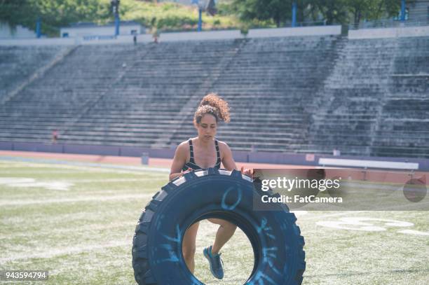 female athlete cross trains with a giant tire on a stadium field - giant camera stock pictures, royalty-free photos & images