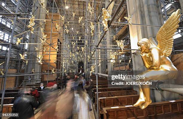 Church visitors walk past one of 300 golden angels attached to scaffolding in the Holy Cross church in the southern German city of Munich on December...