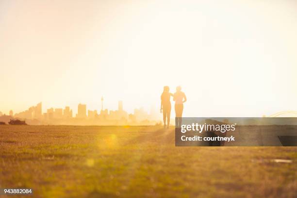 silhouette von 2 frauen im park spazieren. - sunrise city stock-fotos und bilder