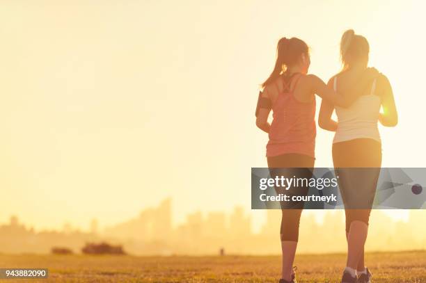 silueta de 2 mujeres caminando en el parque. - sunset freinds city fotografías e imágenes de stock
