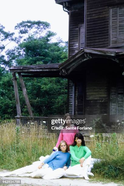 Three models sitting in grass in front of a farm house model in sashed pink cashmere sweater by Braemer, model in apple green wool/nylon sweater by...