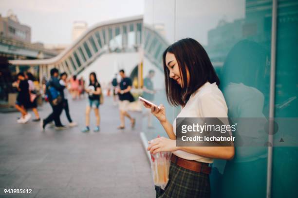 jeune femme asiatique dans le quartier du centre-ville de bangkok, prendre une pause, envoyer des sms sur la cellule tout en sirotant une boisson - sms'en photos et images de collection
