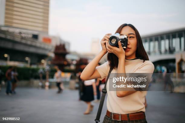 giovane viaggiatrice asiatica nel quartiere del centro di bangkok, con in mano una macchina fotografica vintage - photographing foto e immagini stock