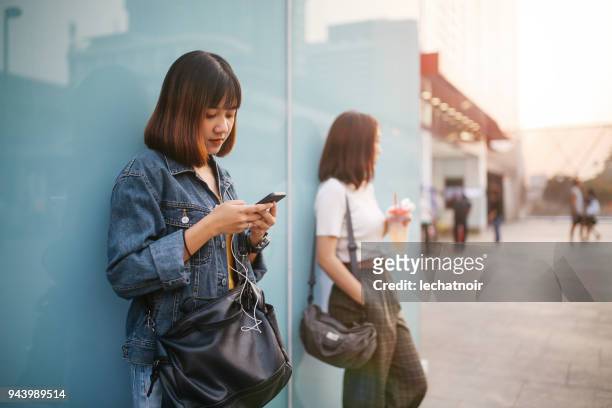 jeunes femmes asiatiques dans le quartier du centre-ville de bangkok, prendre une pause, envoyer des sms sur le téléphone portable, en attente - sms'en photos et images de collection