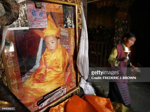 Tibetan pilgrim walks with her butter lamp past a portrait of Beijing's Communist government-appointed candidate for the 11th Panchen Lama, a boy...
