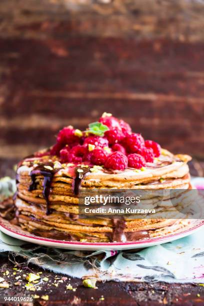 stack of wheat golden pancakes or pancake cake with freshly picked raspberry, chopped pistachios, chocolate sauce on a dessert plate, selective focus - raspberry sauce stock pictures, royalty-free photos & images