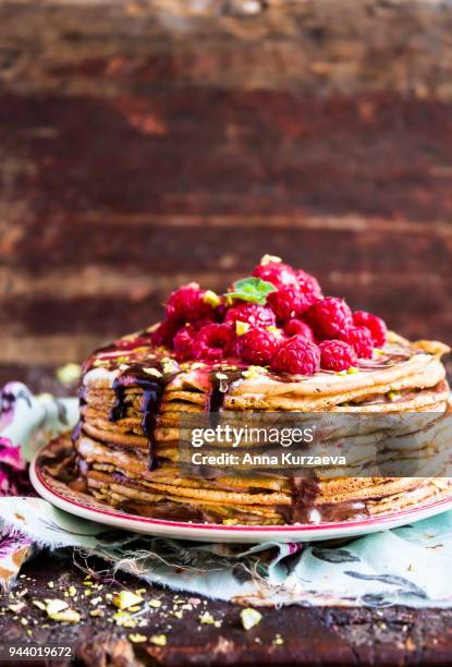stack of wheat golden pancakes or pancake cake with freshly picked raspberry, chopped pistachios, chocolate sauce on a dessert plate, selective focus - raspberry sauce stock pictures, royalty-free photos & images